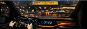Conductor de monovolumen al volante en una carretera mojada cerca del Aeropuerto de Berlín Brandenburg con señales Ankunft y Abflug al atardecer